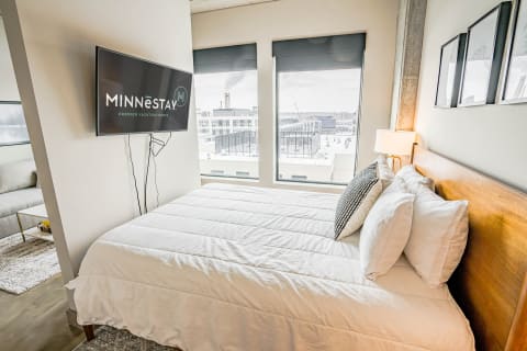 Modern bedroom with a queen-sized bed and flat-screen TV overlooking the city.