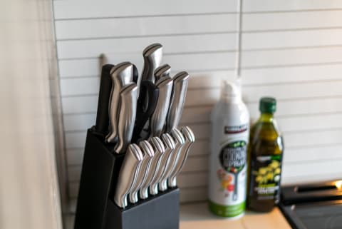 A knife block with various stainless steel knives beside cooking spray and olive oil in a kitchen.