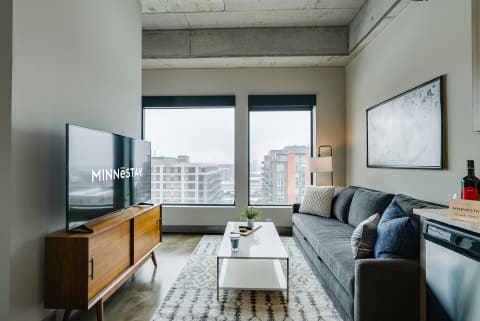 Modern living room with a gray sofa, white coffee table, and large windows overlooking the city.