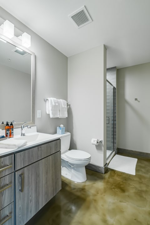 Modern bathroom with a light wood vanity, white towels, and a glass shower.