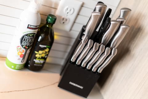 A knife block with stainless steel knives next to canola oil spray and olive oil on a kitchen countertop.