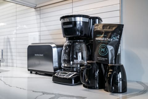 Modern coffee maker setup with black cups and Minnestay coffee on a marble countertop.