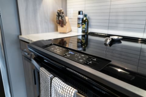 Close-up of a sleek black stovetop with digital controls and kitchen accessories in a modern kitchen setting.