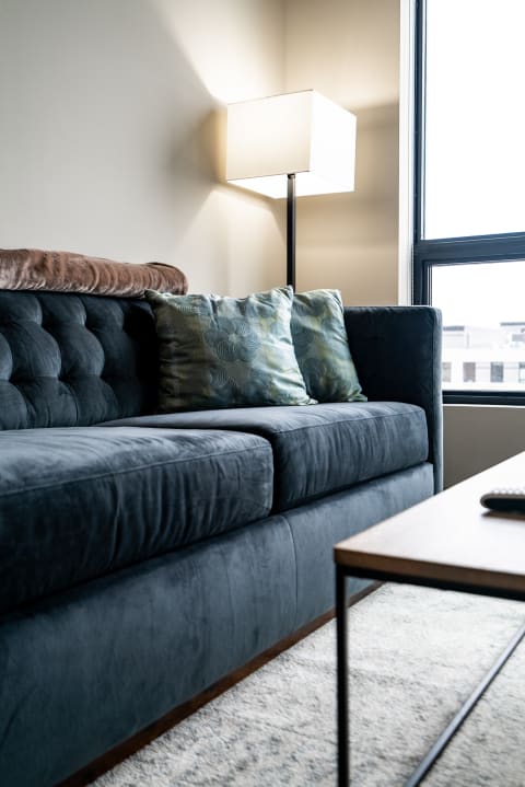 A dark blue tufted sofa with green accent pillows and a floor lamp in a modern living room.