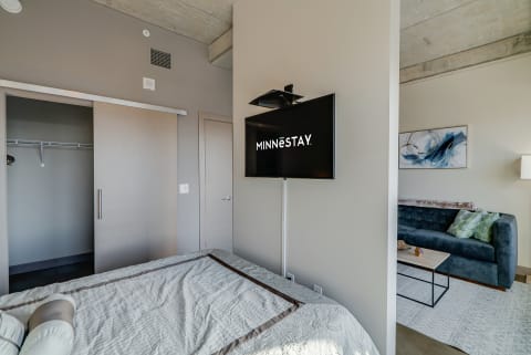 Contemporary bedroom with a bed, mounted TV, and a blue couch in a living area.