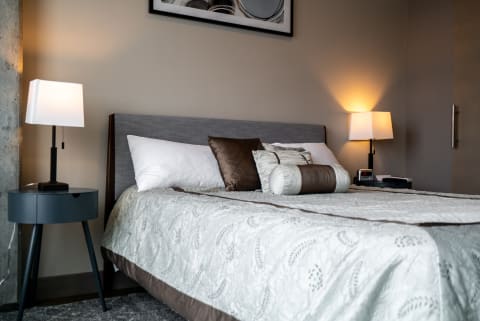 A cozy modern bedroom with a neatly made bed, pillows, and lamps.