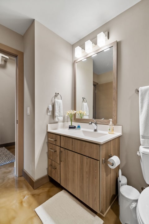 Modern bathroom featuring a wooden vanity, mirror, and stylish lighting.
