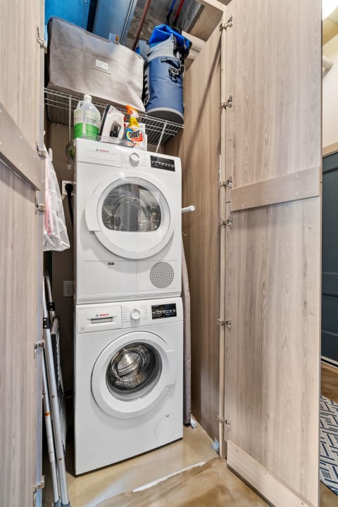 Compact laundry area with Bosch washer and dryer and supplies on a shelf.