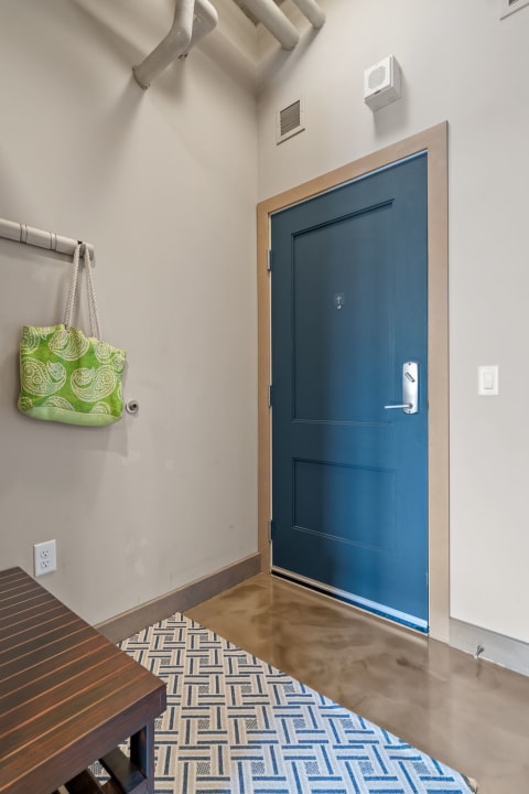 Entryway with a navy blue door, green tote bag, and patterned rug on the floor.