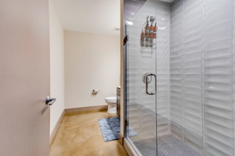 Modern bathroom with glass shower, toilet, and blue bath mat.