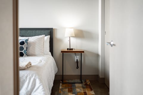A cozy modern bedroom showing a neatly made bed with decorative pillows and a side table with a lamp.