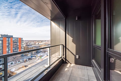 Modern balcony with a city view featuring sleek black paneling and bright sky.