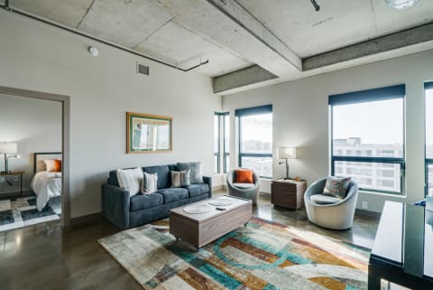 A contemporary living room featuring a gray sofa, colorful pillows, and large windows with city views.