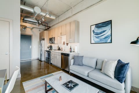 A modern apartment interior with a sofa, kitchen, and dining area.