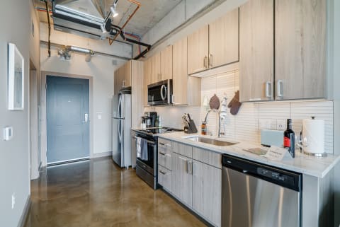 Contemporary kitchen with light wood cabinets, stainless steel appliances, and polished concrete floor.