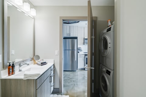 A bathroom with a white vanity and a view into a kitchen with stainless steel appliances.