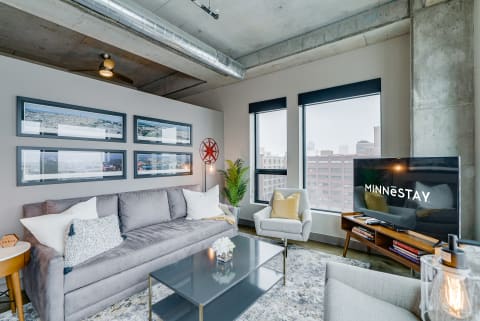 A modern loft living room featuring gray couch, decorative pillows, and large windows with city views.