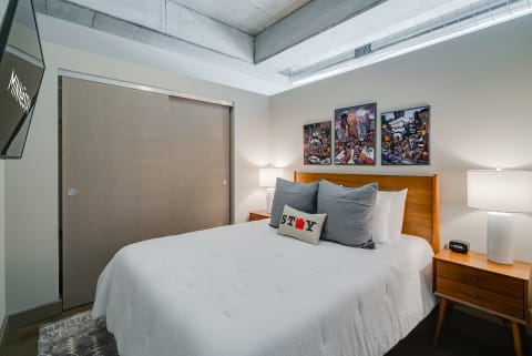 A modern bedroom featuring a queen bed, decorative pillows, and city-themed art.