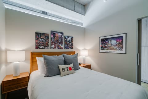 A cozy bedroom featuring a bed with decorative pillows, bedside lamps, and urban art on the walls.