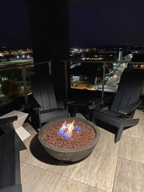 Nighttime balcony with a fire pit and city lights below.