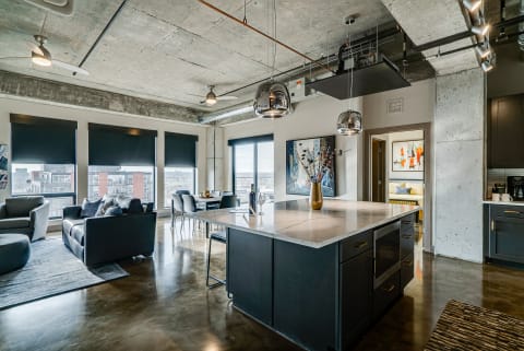 A stylish modern apartment with a kitchen island, seating areas, and large windows offering a city view.