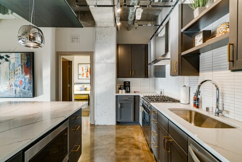 Modern kitchen featuring dark cabinets, a marble island, and stainless steel appliances.