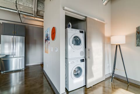 A contemporary laundry area featuring a stacked washer and dryer, a stainless steel refrigerator, and a minimalist lamp.