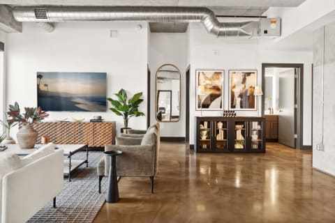 A contemporary living room with a sofa, armchair, artwork, and a view of the beach on a TV.
