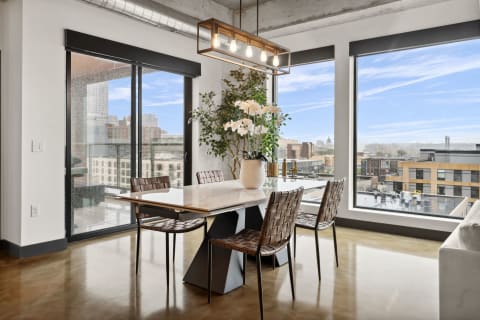 Contemporary dining space featuring a marble table, woven chairs, and large windows with urban views.