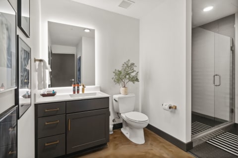 A modern bathroom with dark vanity, backlit mirror, and sleek shower enclosure.