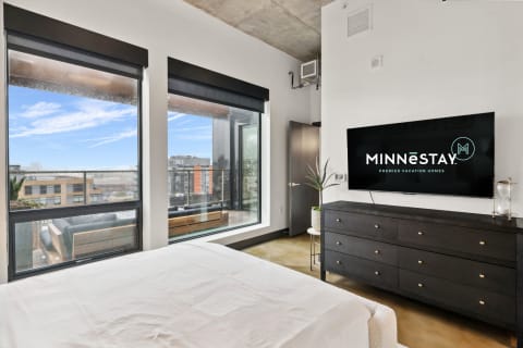 Modern bedroom with large windows, a flat-screen TV, and a stylish dresser.