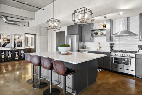 Modern kitchen featuring a marble island, leather bar stools, and stainless steel appliances.