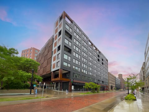 A modern building with a sleek design surrounded by greenery and a wet street.
