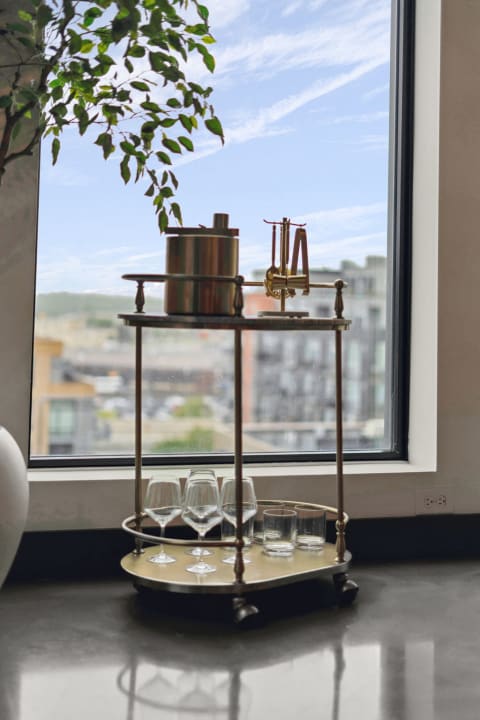 Stylish bar cart with glasses near a large window with a cityscape view.