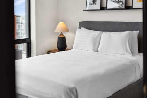 A modern bedroom featuring a neatly made bed, a lamp, and framed pictures above the bed.