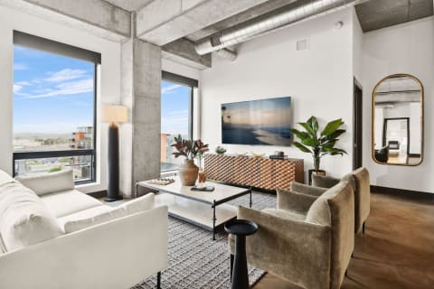 Stylish modern living room with large windows, a white sofa, green armchairs, and contemporary decor.