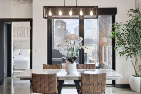Modern dining area with a sleek table, designer chairs, an orchid centerpiece, and a city view through rain-soaked glass.
