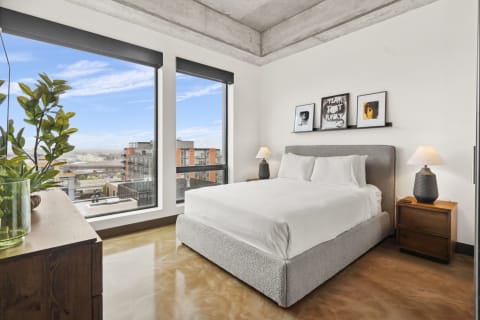 Modern bedroom with large windows, a plush bed, and artistic decor.