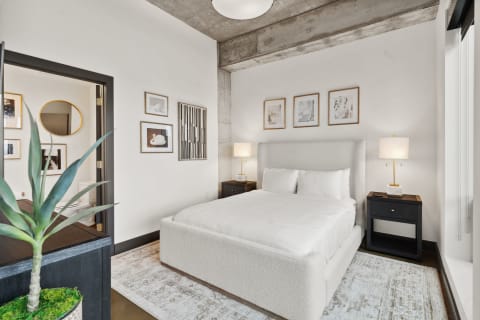 Modern bedroom with a white bed, black nightstand, and contemporary wall art.