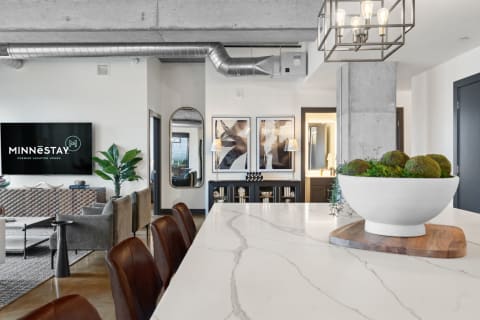 Interior view of a modern kitchen and living area, showing a marble island, leather stools, and contemporary decor.