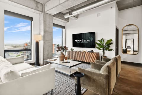 Modern living room with large windows, a light sofa, dark armchairs, and geometric wood decor.