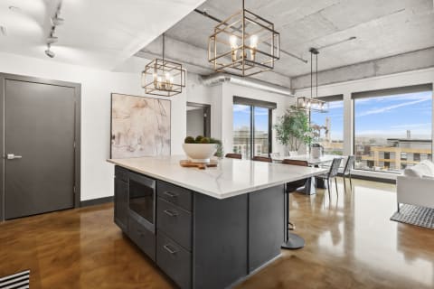 Open-concept kitchen and dining area with a marble island, modern lighting, and large windows.