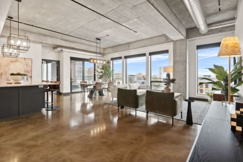 Modern loft-style living room with exposed concrete and large windows overlooking the city.