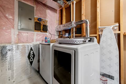 Laundry room with a dryer, washer, and ironing board in a basement.