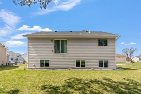 Side view of a beige suburban house with a green lawn and blue sky.