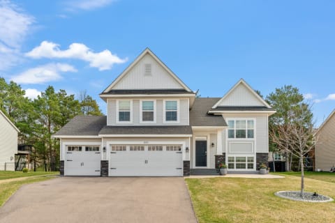 Modern house with light siding and stone accents, featuring a dark front door and two garage doors.