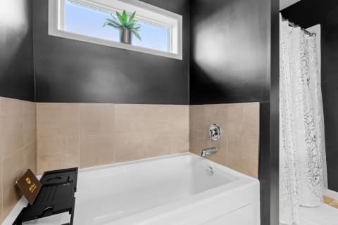 Modern bathroom with a white bathtub, black walls, beige tiles, and a floral shower curtain.