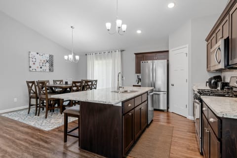 Modern kitchen with dark wood cabinets, granite countertop, and dining area with rectangular table and abstract wall art.