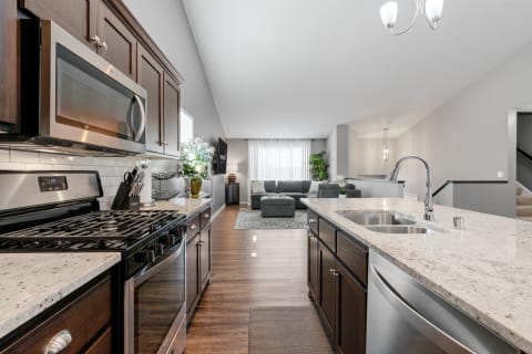 View of a contemporary kitchen leading into a living room with a gray sofa and natural light.