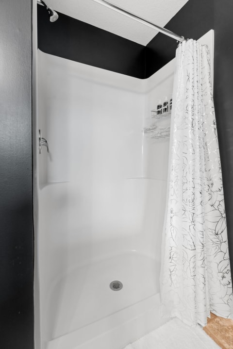 A modern shower with white walls, black accents, and a floral shower curtain.